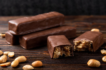 Chocolate bar with caramel and peanut on dark wooden background.  - obrazy, fototapety, plakaty