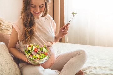 Pregnancy and healthy organic nutrition. Pregnant woman enjoying fresh vegetable salad in bed, free space. Concept of expectation and health.