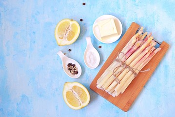 Obraz na płótnie Canvas Ingredients for cooking asparagus on a light blue concrete background: fresh white asparagus, lemon, butter, salt, pepper. Top view, copy space.