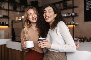 Two cheerful young girls friends standing at the cafe