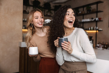 Two cheerful young girls friends standing at the cafe