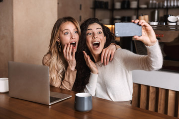 Two cheerful young girls friends sitting at the cafe table