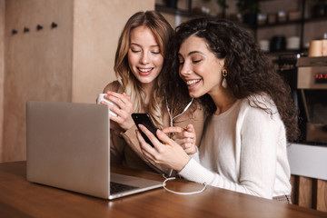 Two cheerful young girls friends sitting at the cafe table