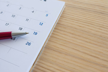 calendar page on wood table background with pen point at 19th date