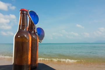 Brown beer bottles and blue sunglasses on a table on the background of the sea and sky