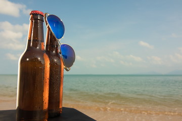Brown beer bottles and blue sunglasses on a table on the background of the sea and sky