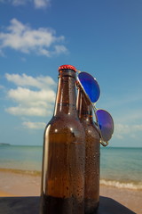 Brown beer bottles and blue sunglasses on a table on the background of the sea and sky