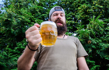 In playful mood. Brutal hipster with winking face having craft beer. Man drinker holding beer mug. Bearded man enjoy drinking beer on nature. Fun loving beer