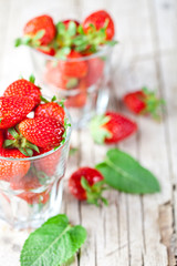 Organic red strawberries in two glasses and mint leaves on rustic wooden background.