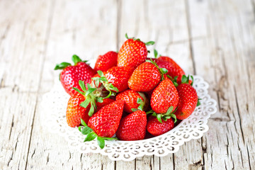 Organic red strawberries on white plate on rustic wooden background.