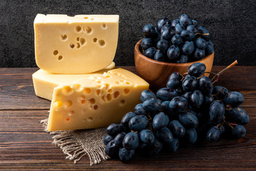 Blue grapes and cheese on dark wooden background.