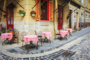 Fototapeta na wymiar Outdoor cafe in the old town. Summer cafe in the narrow old street. Vintage tables on narrow paved street among houses and between walls in Lviv, Ukraine. Concept - travel, landmarks