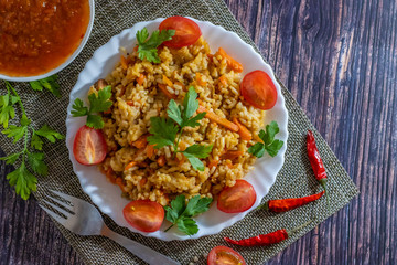 Pilaf and cherry tomatoes in a plate on a wooden background, adjika. Central Asian cuisine. Horizontal orientation. Hot peppers