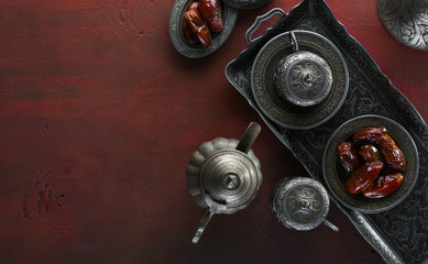 Top view on silver plate with date fruits and coffee cups on the dark red wooden background. Ramadan background. Ramadan kareem.