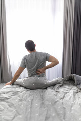 Young Man suffering from back pain after wake up at home in the bedroom.