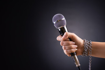 Woman hand with microphone tied with a chain, depicting the idea of freedom of the press or freedom...