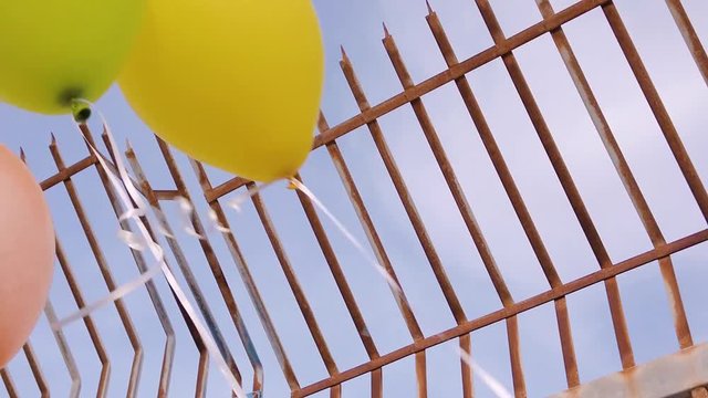 Palloncini di elio colorati che sventola di fianco un cancello a sbarre dritte.