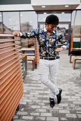 Attractive and handsome stylish indian man wear on shirt and sunglasses standing in the terrace of modern lounge cafe at his work break, his looking time at watches.