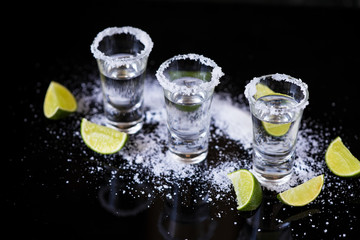 Tequila shot with lime and salt on black background