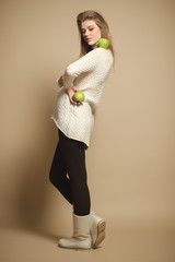 Attractive pregnant girl model in a sweater and warm shoes posing in a studio with apples and greens.