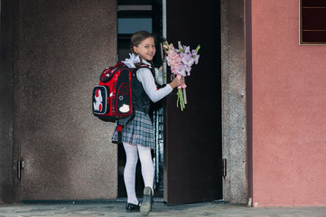 Girl in school uniform with a bouquet of flowers and a backpack on her back is standing on the school stairs