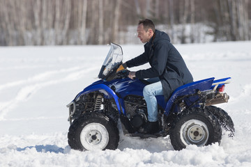 A winter forest in daylight. A man riding a big blue snowmobile
