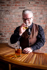Man tasting whisky on a Bar in Front of a red stone wall