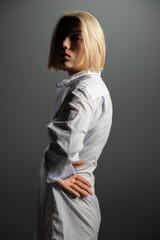 Fashion model. Young blond woman posing in studio wearing white shirt. Beautiful caucasian girl over gray background