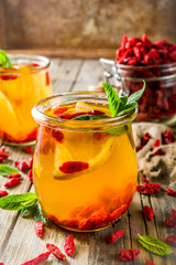 Homemade goji hot tea with mint and lemon slices, wooden rustic background copy space