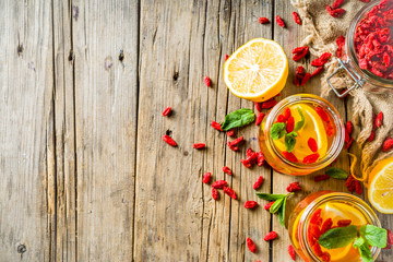 Homemade goji hot tea with mint and lemon slices, wooden rustic background copy space