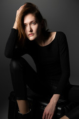 Fashion model. Young woman posing in studio wearing black with boots. Beautiful caucasian girl over gray background