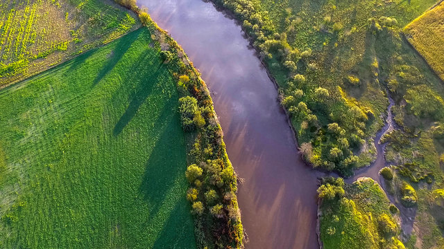 Aerial view of a winding river through green fields and trees