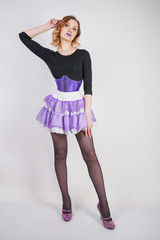 Pretty fashionable blonde girl wearing black jumpsuit with mesh pantyhose and purple corset on white background