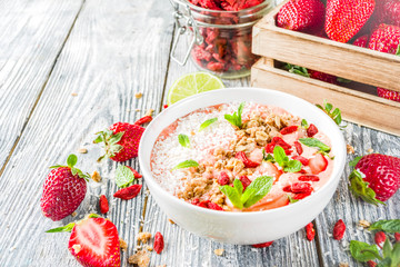Healthy breakfast smoothie bowl with goji and strawberry berries, granola, yogurt, coconut, lime, wooden background copy space