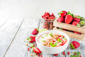 Obraz na płótnie Canvas Healthy breakfast smoothie bowl with goji and strawberry berries, granola, yogurt, coconut, lime, wooden background copy space
