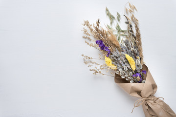 Spring bouquet of dried flowers and herbs wrapped in craft paper on white background with copyspace.