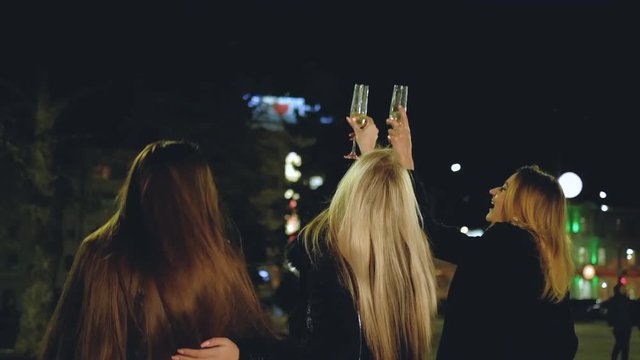 Girls party life. Female friends celebrating special occasion, drinking champagne, walking down the street with night city lights.