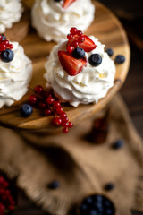 Four homemade white mini desserts pavlova on wooden cake stand with whipped cream and assorted berries