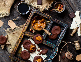 Overhead shot of homemade chocolate tasty cookies with caramel or condensed milk on dark blue wooden board with copper cup with caramel on rustic table