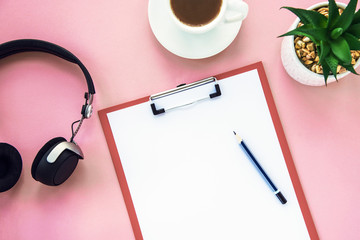 A cup of coffee, a notebook with pencil, succulent and headphones on a pink background. Cosy workspace. Top view, flat lay.