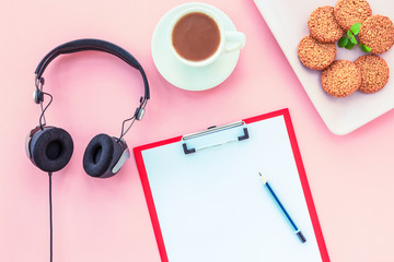 A cup of coffee, rice crackers, notebook with pencil and headphones on a pink background. Cosy workspace. Top view, flat lay.