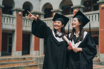 asian university college graduate student woman in graduation academic dress gown smiling pointing...