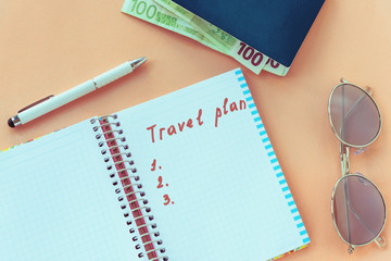 Notebook with the words "Travel plan", pen, sunglasses, passport and money on a pink background. Prepare for travel concept. Top view, flat lay.