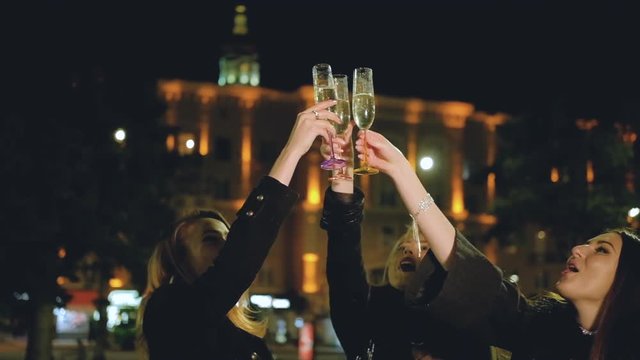 Girls party. Female friends having fun, clinking glasses with champagne on the street with night city lights.