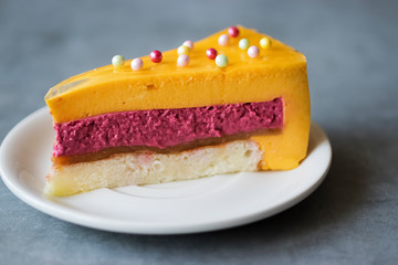 A piece of mousse cake with a taste of mango and strawberry on a white plate.