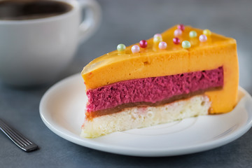 A piece of mousse cake with a taste of mango and strawberry on a white plate and a cup of coffee.