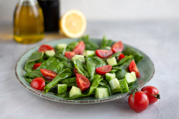 Salad of greens, cucumbers, cherry tomatoes with lemon, olive oil and soy sauce in a green plate with a gray background