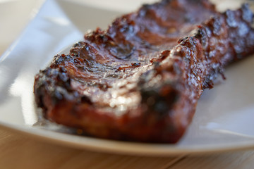 Close up of grilled and barbecued pork ribs on a white plate. Side view.