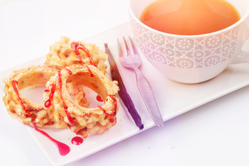 Breakfast with a cup of tee and a cake with jam on a white plate and background