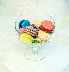 bright colored and marbled macaroons in glass vase on white brick background.